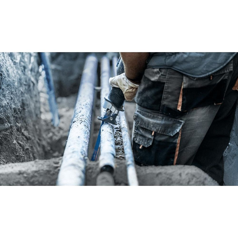 Pracownik tnie niebieską rurę piłą w wykopie.