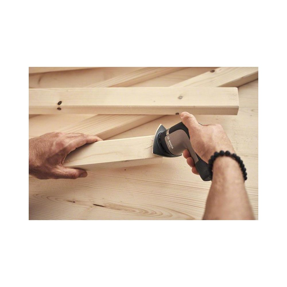 Ein Mann schleift Holz mit einem Dreieckschleifer. Mehrere Holzplanken liegen im Hintergrund.