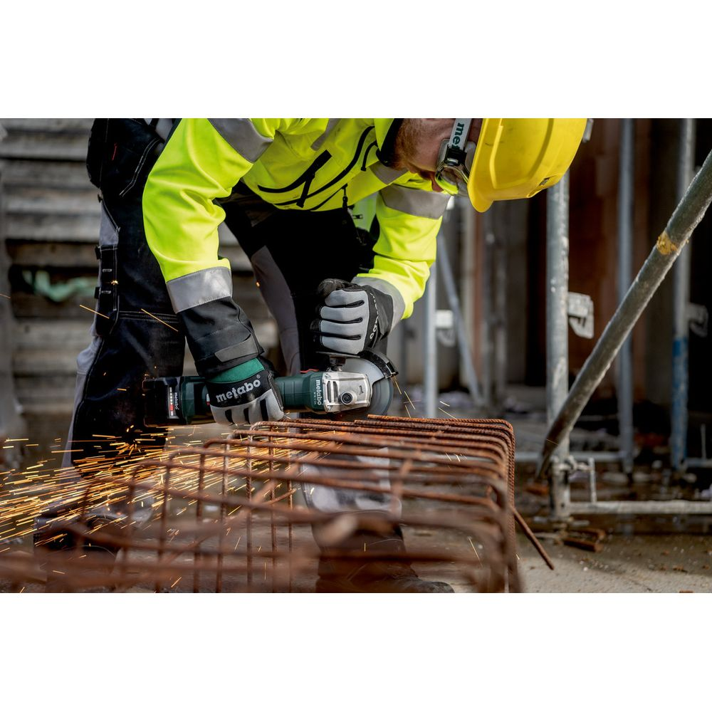 Un ouvrier du bâtiment avec un casque jaune utilise une meuleuse d'angle sur des barres métalliques.
