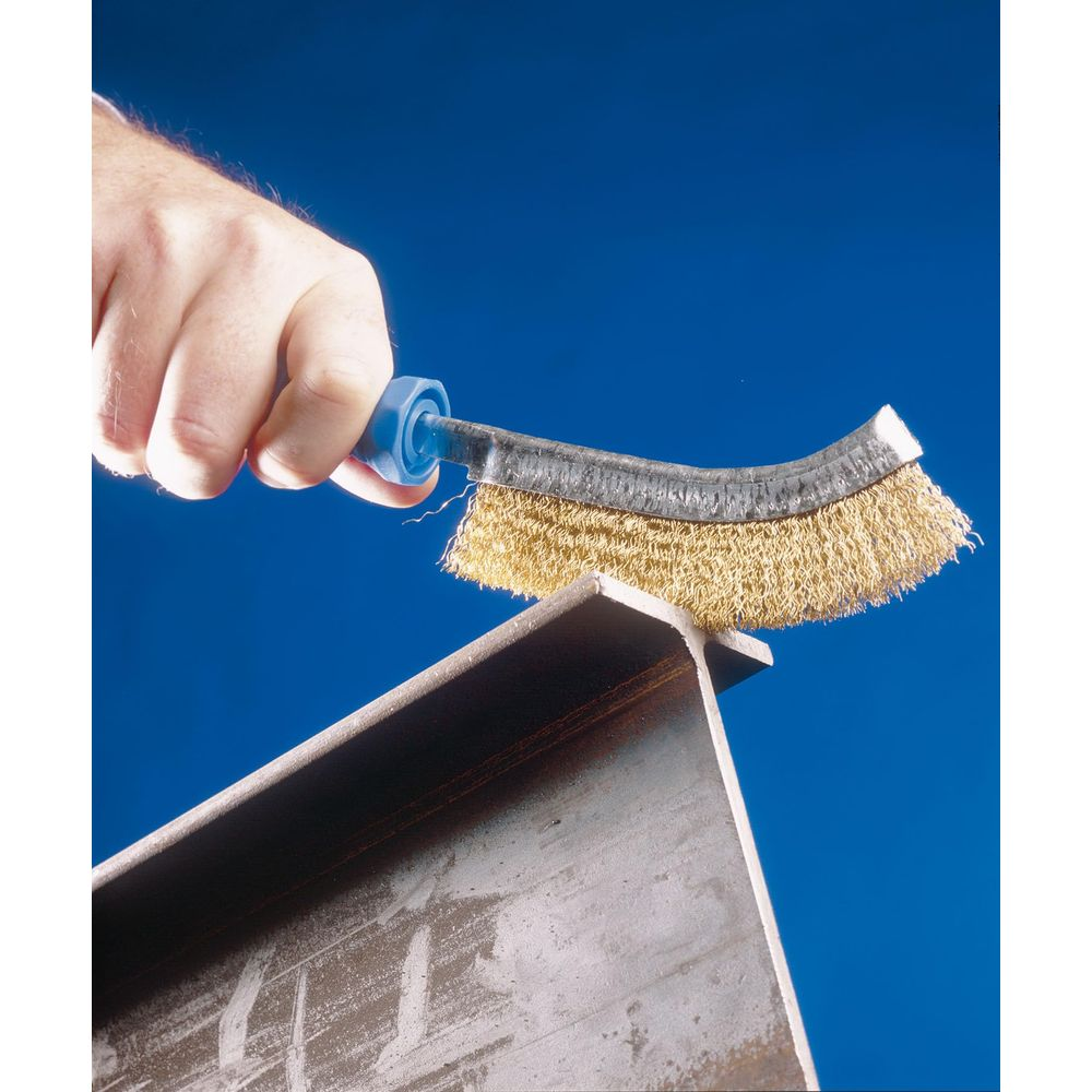 Eine Hand hält eine Drahtbürste über einem Metallträger vor blauem Himmel.