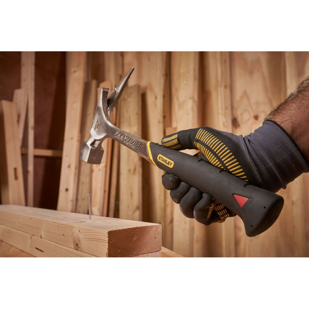 Mano con guanto tiene martello sopra chiodo in legno.