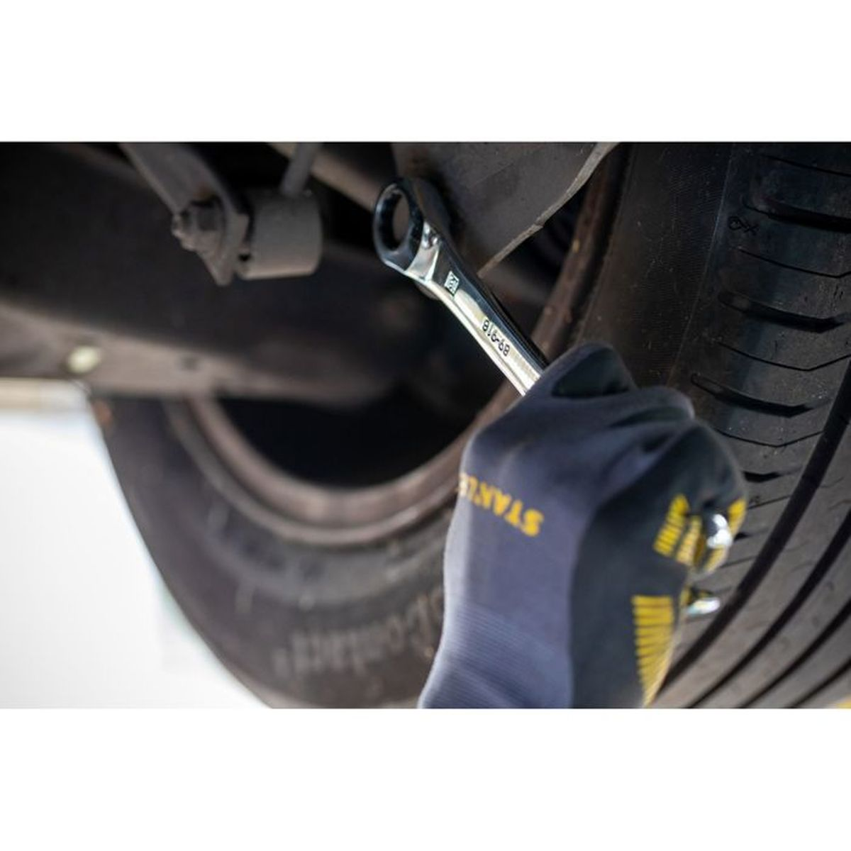 Una mano guantata usa una chiave su un componente della sospensione dell'auto vicino alla ruota.