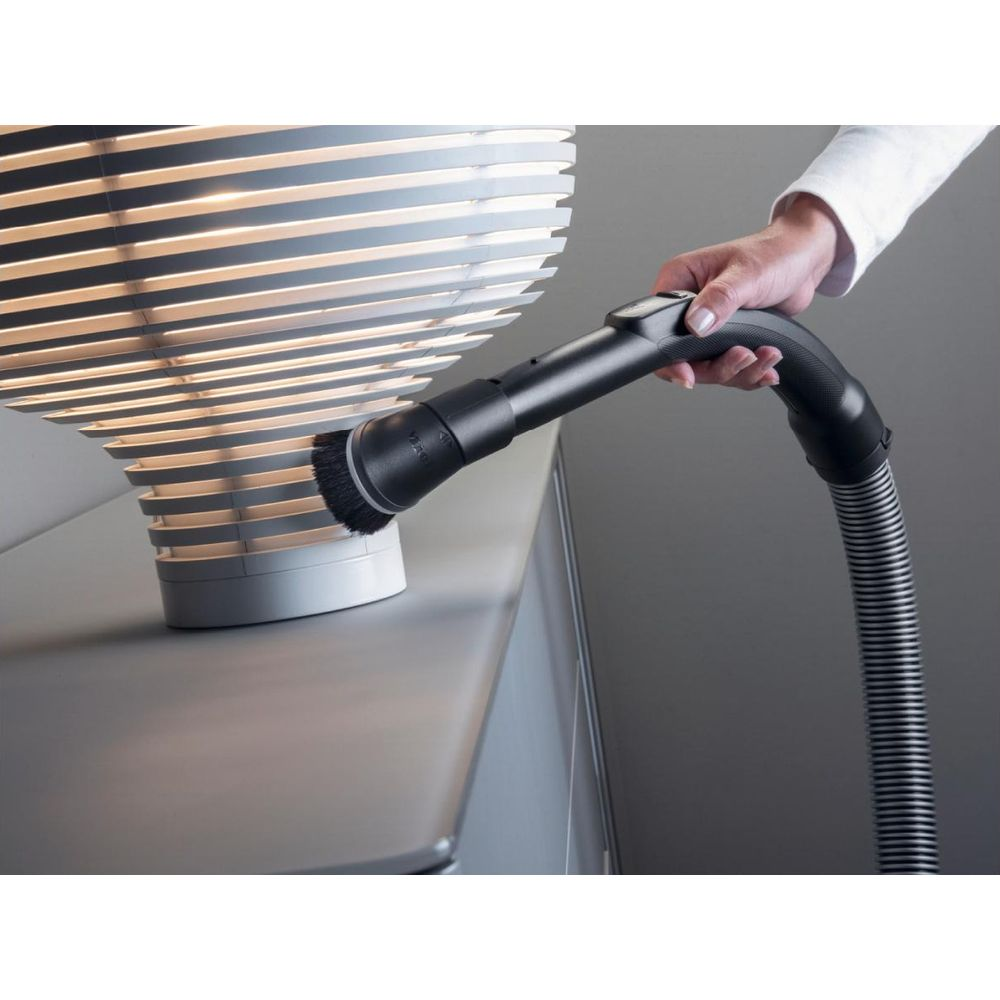 Eine Hand benutzt einen Staubsauger mit Bürstenaufsatz, um eine Lampe zu reinigen.