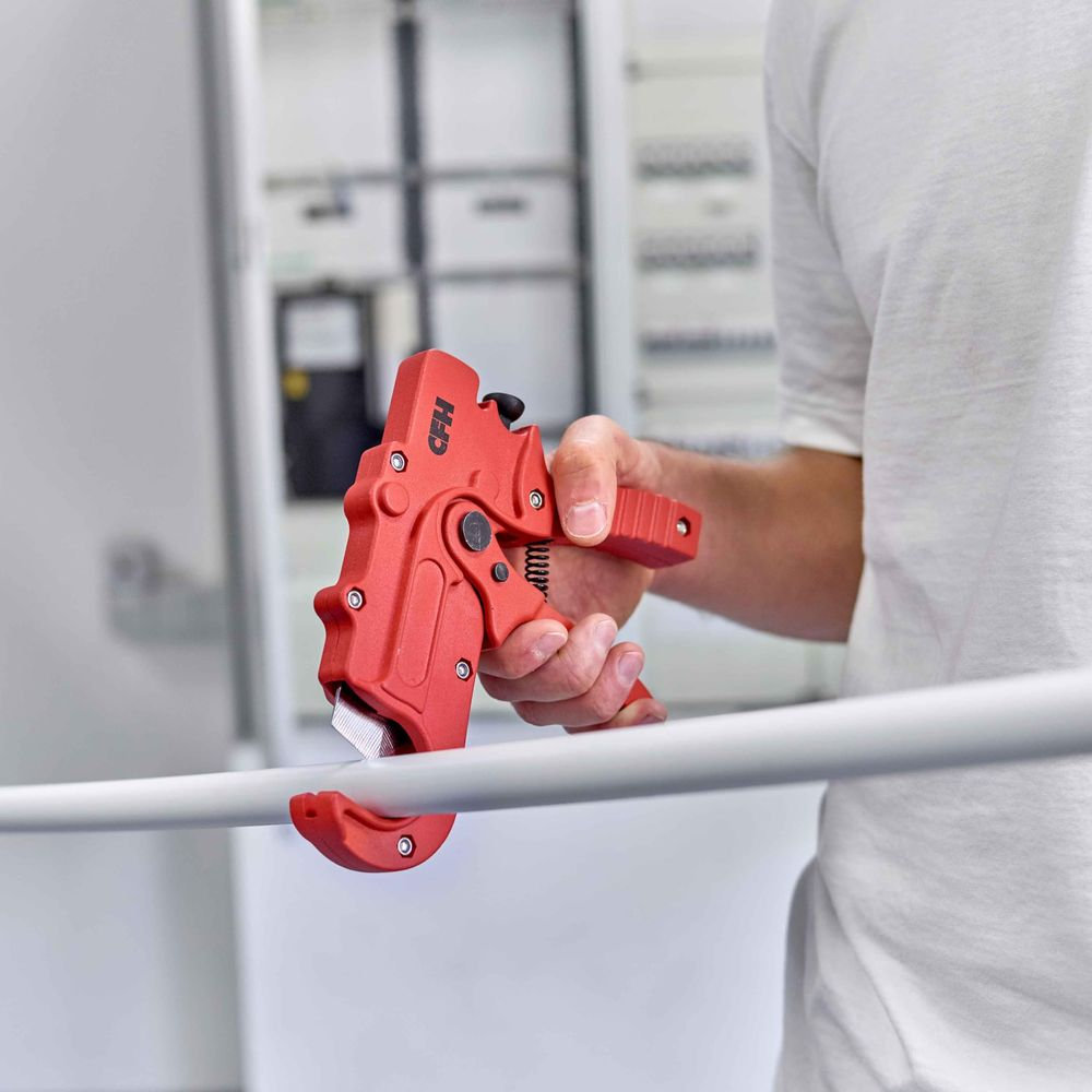 Persona che tiene un tagliatubi rosso, taglia un tubo bianco davanti a un pannello di controllo.