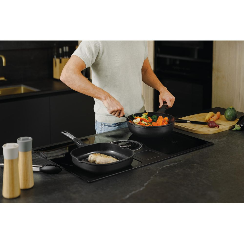 Man cooks vegetables and fish in a modern kitchen on an induction cooktop.