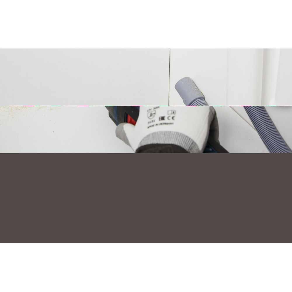 Dłoń w białej rękawicy trzyma wiertarkę tworzącą kurz.