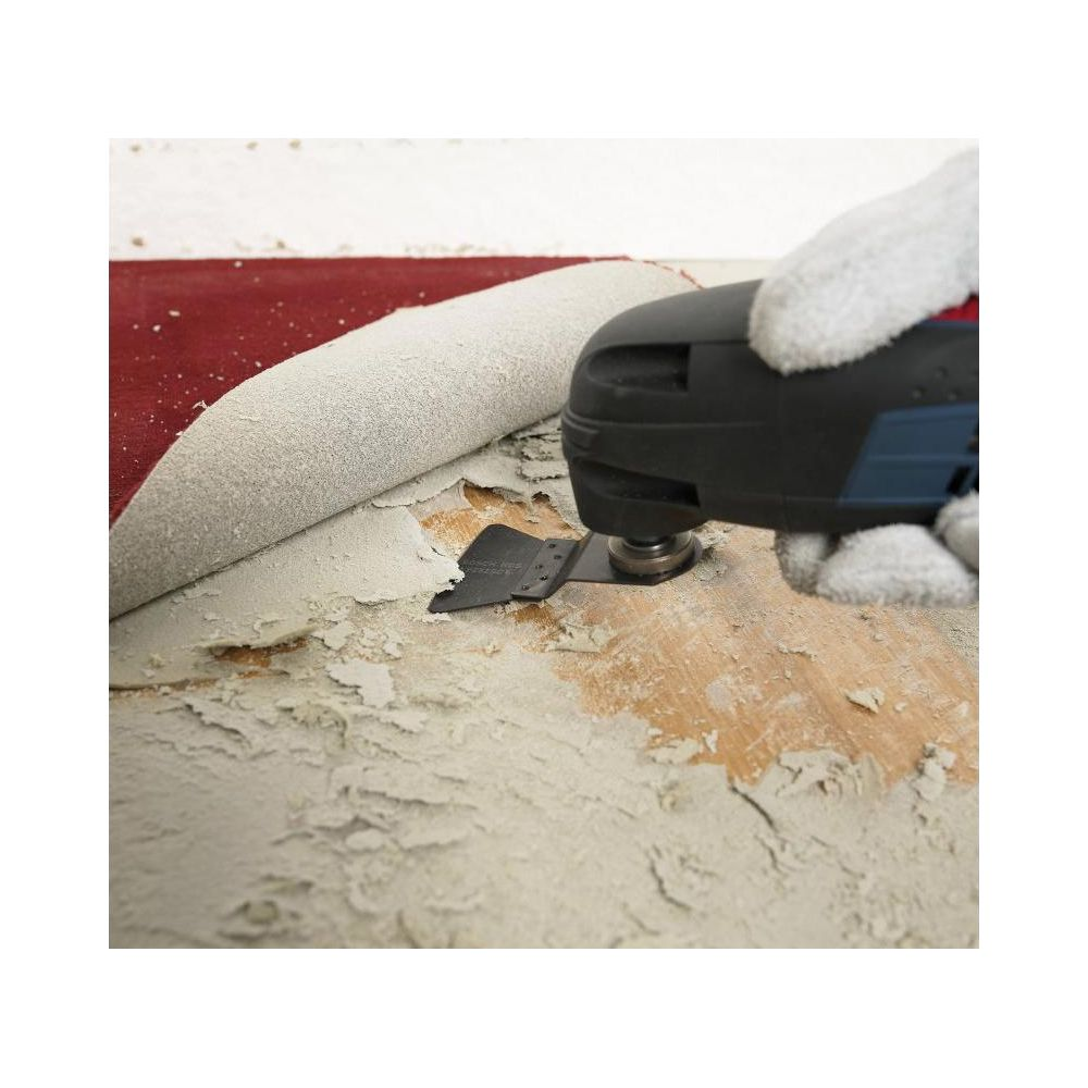 Narzędzie wielofunkcyjne zeskrobuje dywan z drewnianej podłogi.