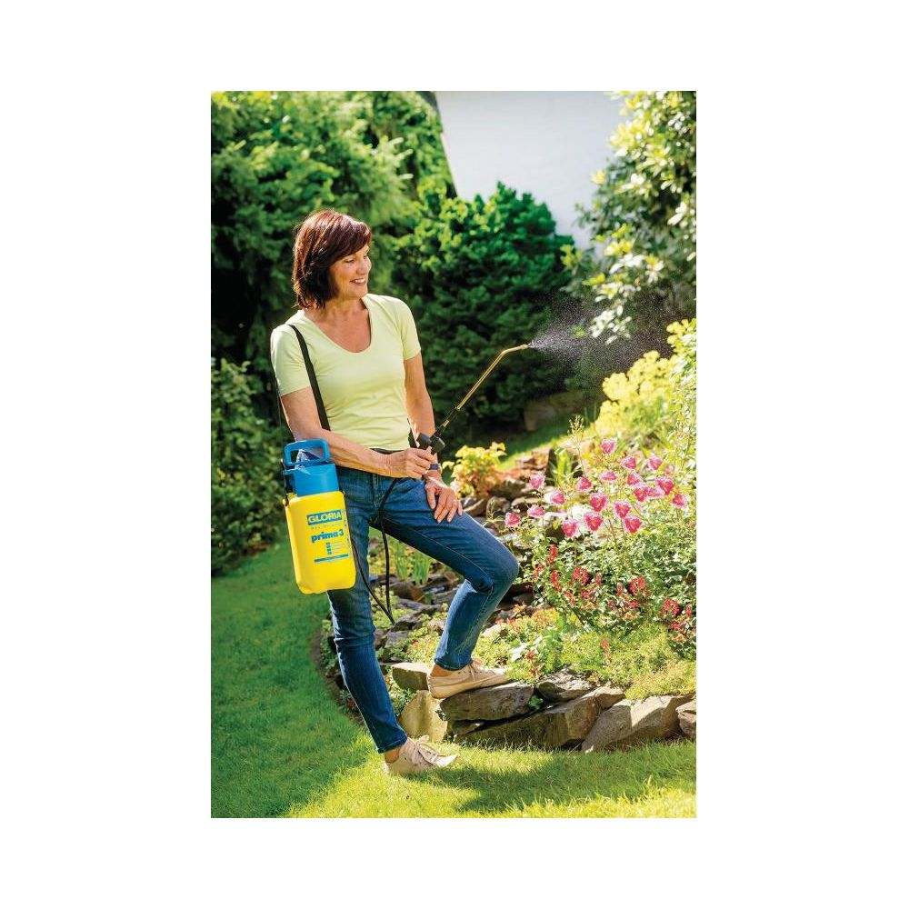 Frau besprüht Blumen mit gelb-blauem Sprüher in einem Garten.