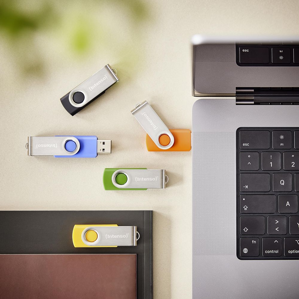 Kilka kolorowych pendrive'ów rozrzuconych obok otwartego laptopa.