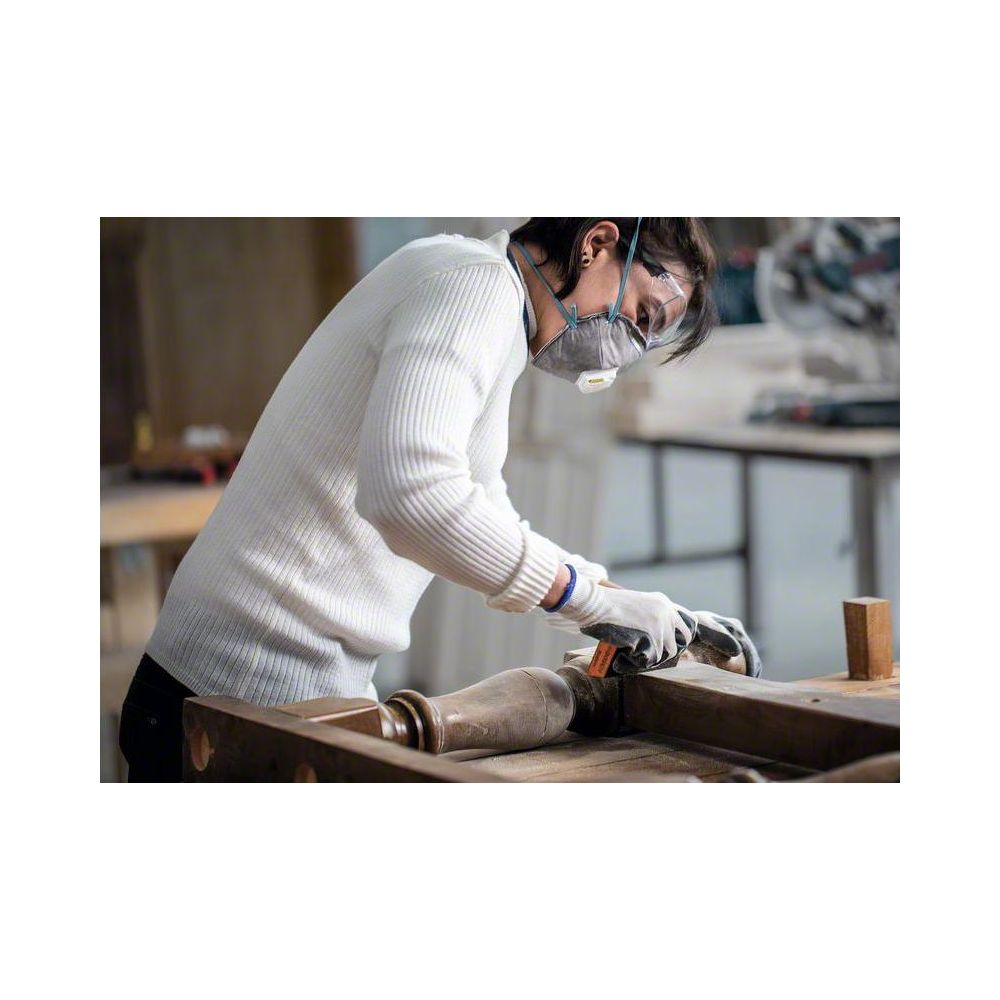 Eine Person mit Maske und Schutzbrille schleift ein Holzmöbelstück.