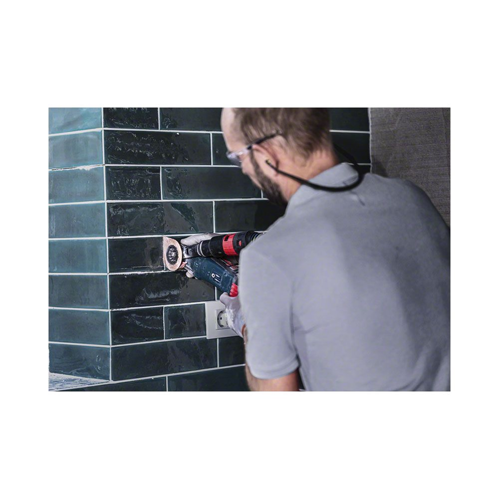 Mann mit Werkzeug bearbeitet geflieste Wand neben Steckdose.