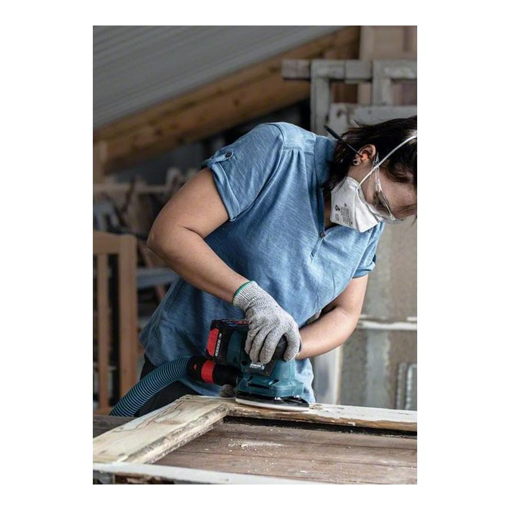 Eine Person schleift Holz mit einem Schleifgerät, trägt Handschuhe und eine Maske.