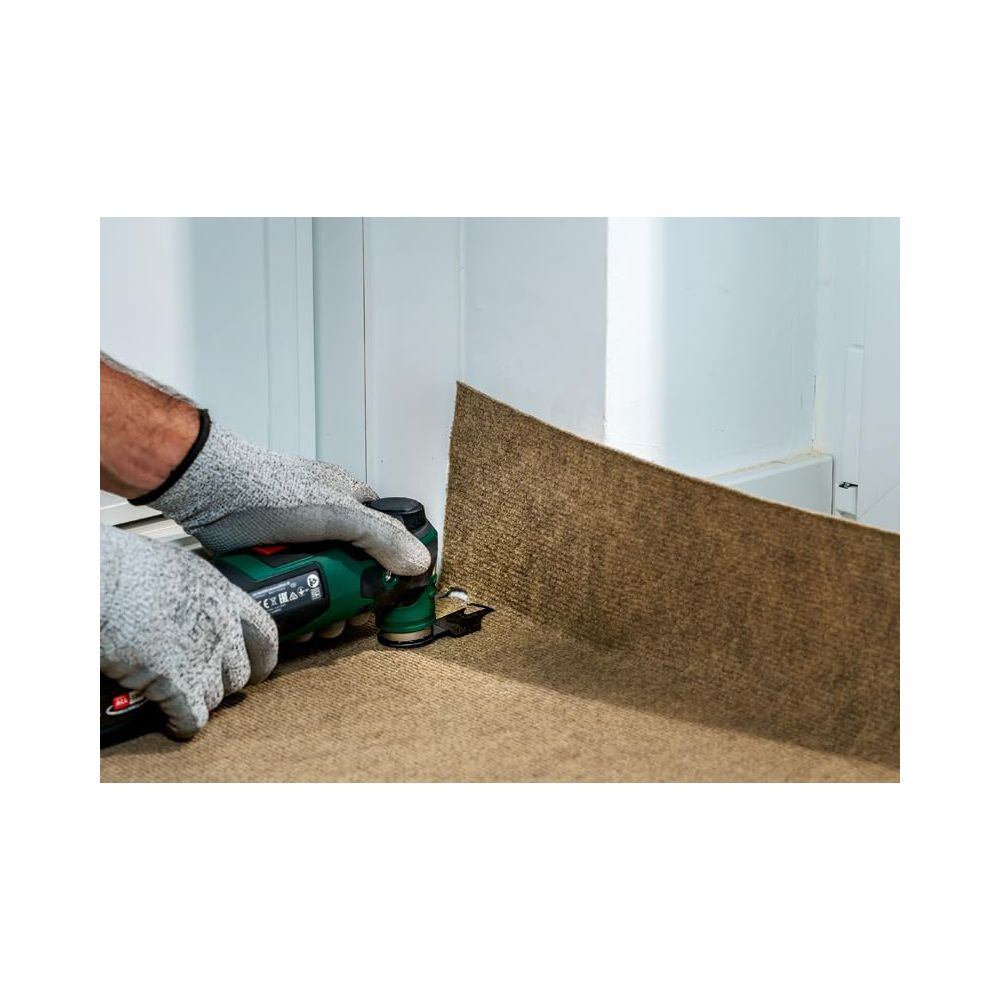 Ręce w rękawiczkach tną dywan narzędziem przy ścianie.