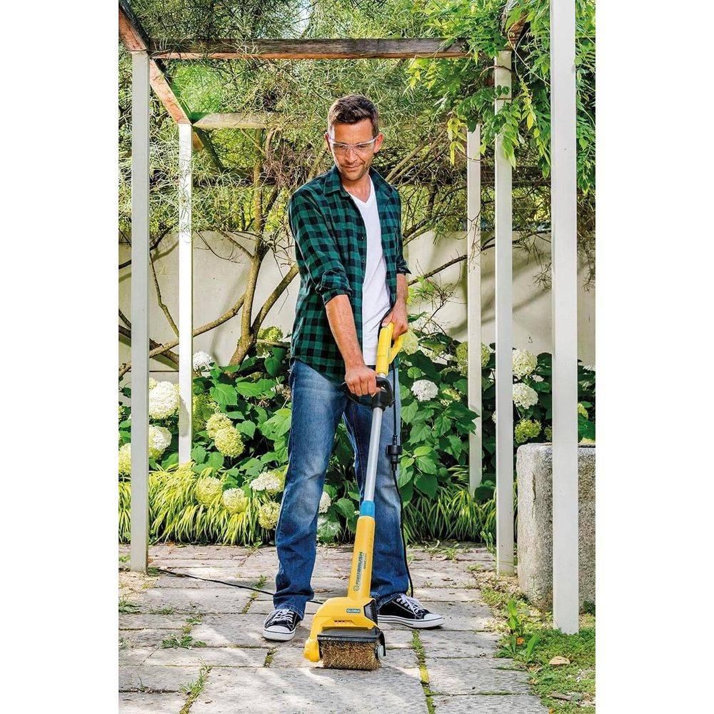Mann reinigt Weg mit elektrischer Bürste im Garten.