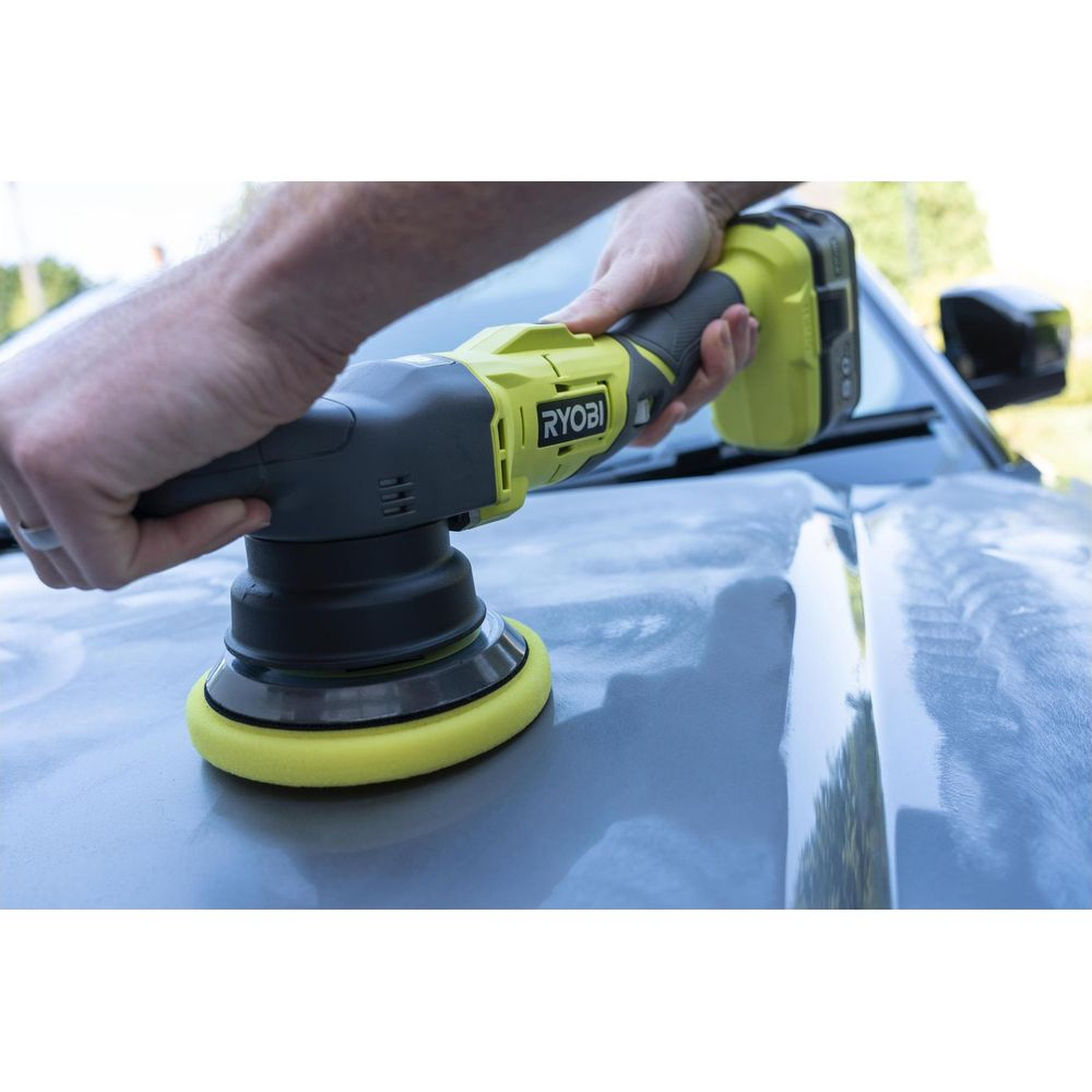 Eine Hand hält einen gelben und grauen Ryobi Polierer, der auf der Motorhaube eines Autos verwendet wird.