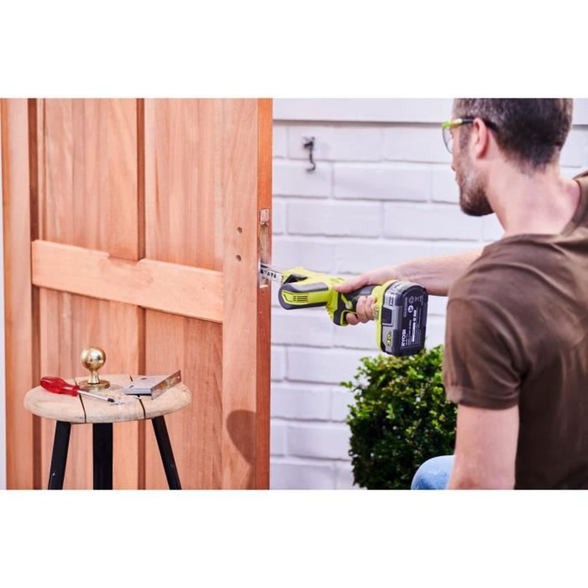 Hombre usa sierra sable en puerta de madera. Herramientas en taburete.