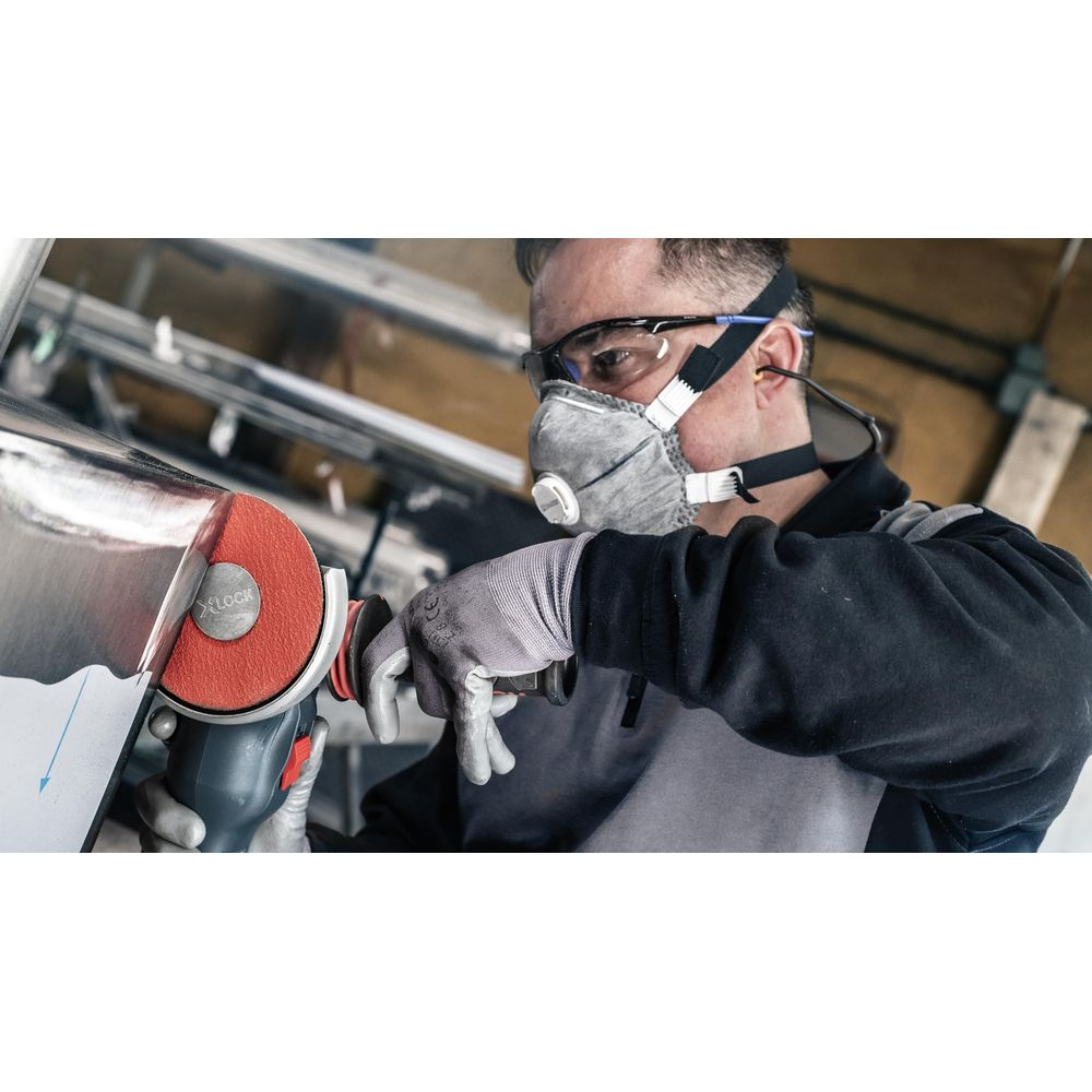Mann mit Schutzmaske schleift Metall mit einem Winkelschleifer in einer Werkstatt.