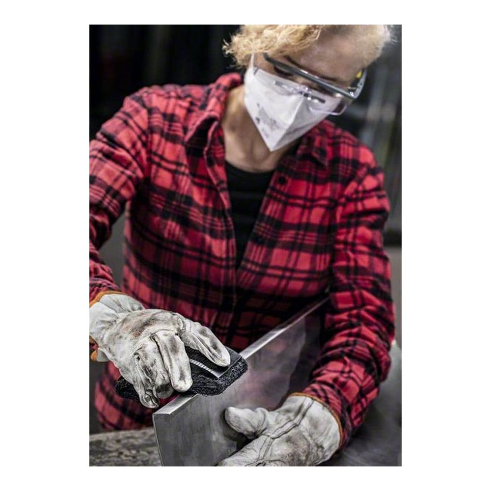 Eine Person mit Schutzmaske und Brille bürstet Metallteile.