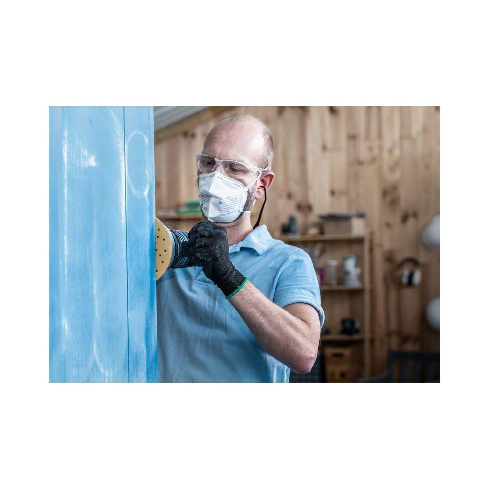 Mann schleift blaues Objekt mit Schutzmaske und Brille.