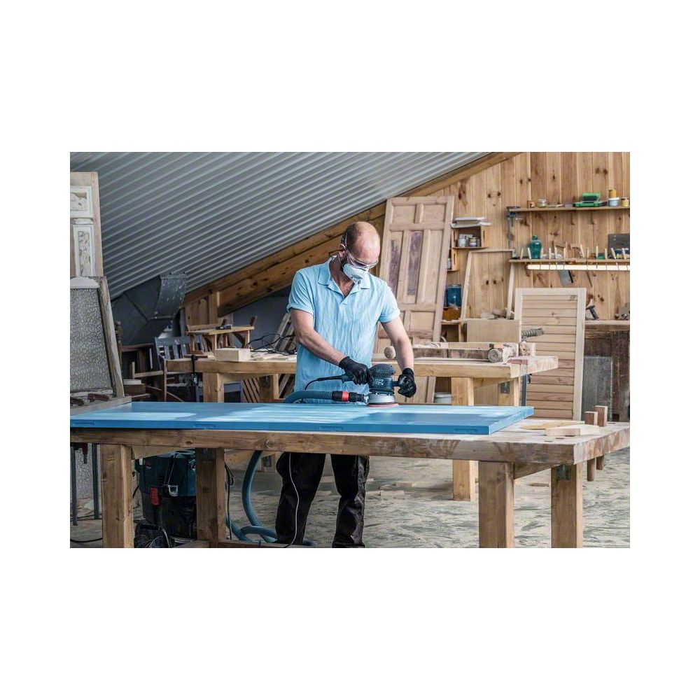 Mann schleift blaue Holzplatte in Werkstatt mit Staubabsaugung.