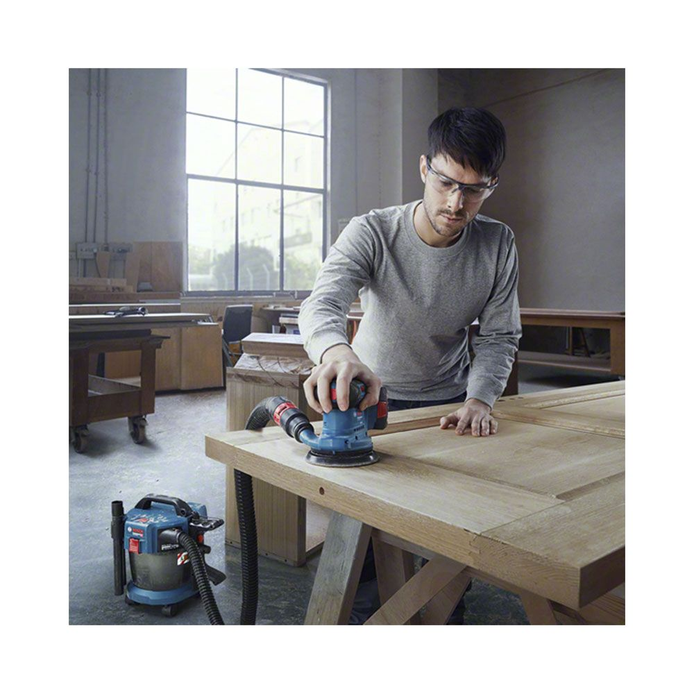Mann schleift Holz im Werkstatt. Blaue Schleifmaschine mit Staubsauger.