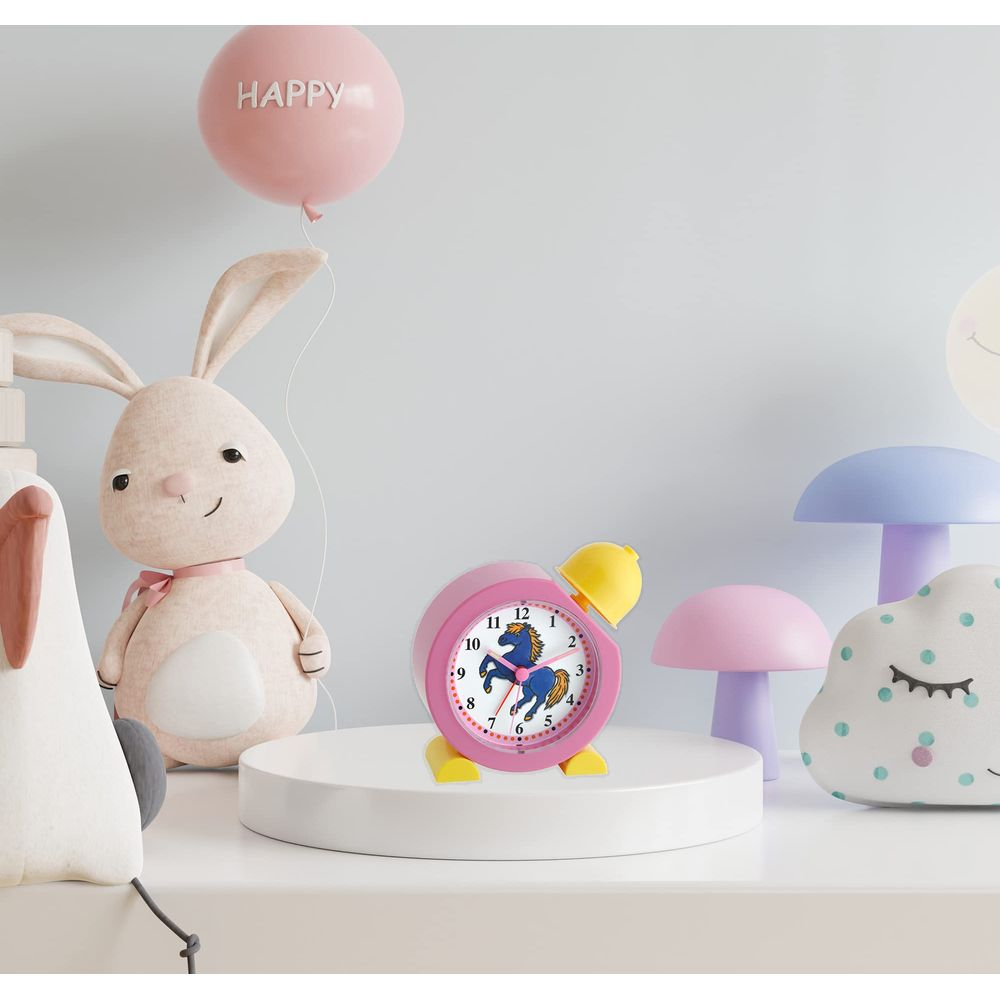 Un réveil rose avec une licorne est posé sur une plateforme blanche, à côté d'un lapin en peluche.