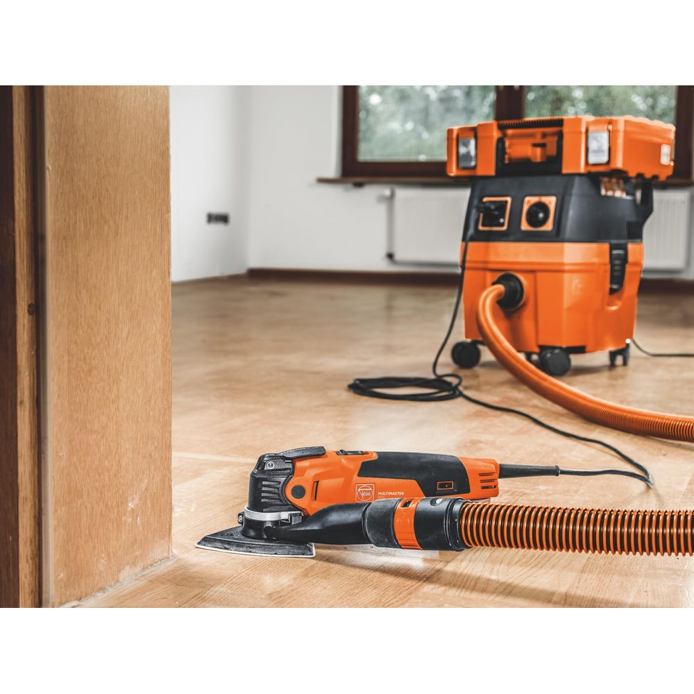 Ein orangefarbener Schleifer liegt auf einem Holzboden vor einem orangefarbenen Staubsauger.