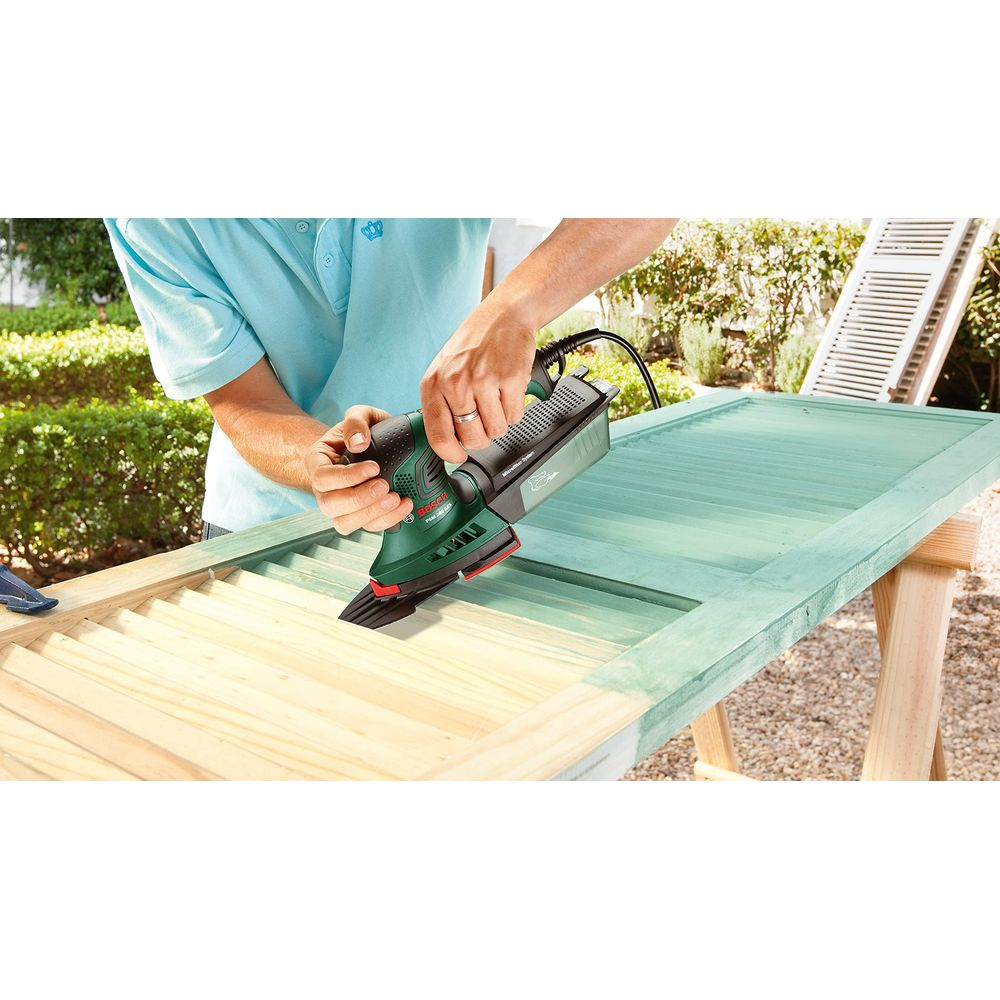 Uomo leviga una porta di legno verde acqua con levigatrice Bosch verde all'aperto.