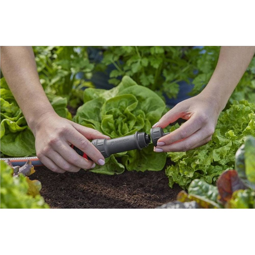 Handen verbinden tuinslangkoppeling naast sla.