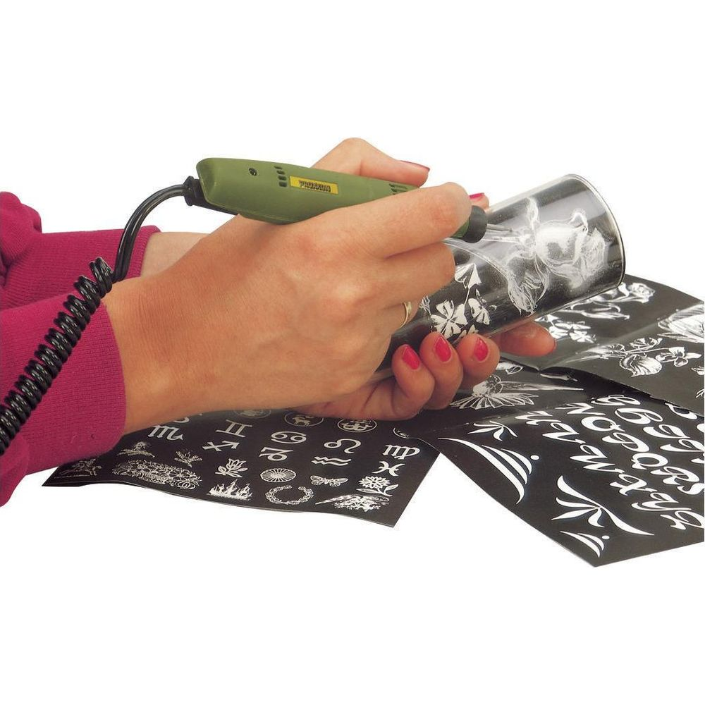 Person graviert Glas mit Werkzeug, Schablone mit Sternzeichen und Buchstaben daneben.