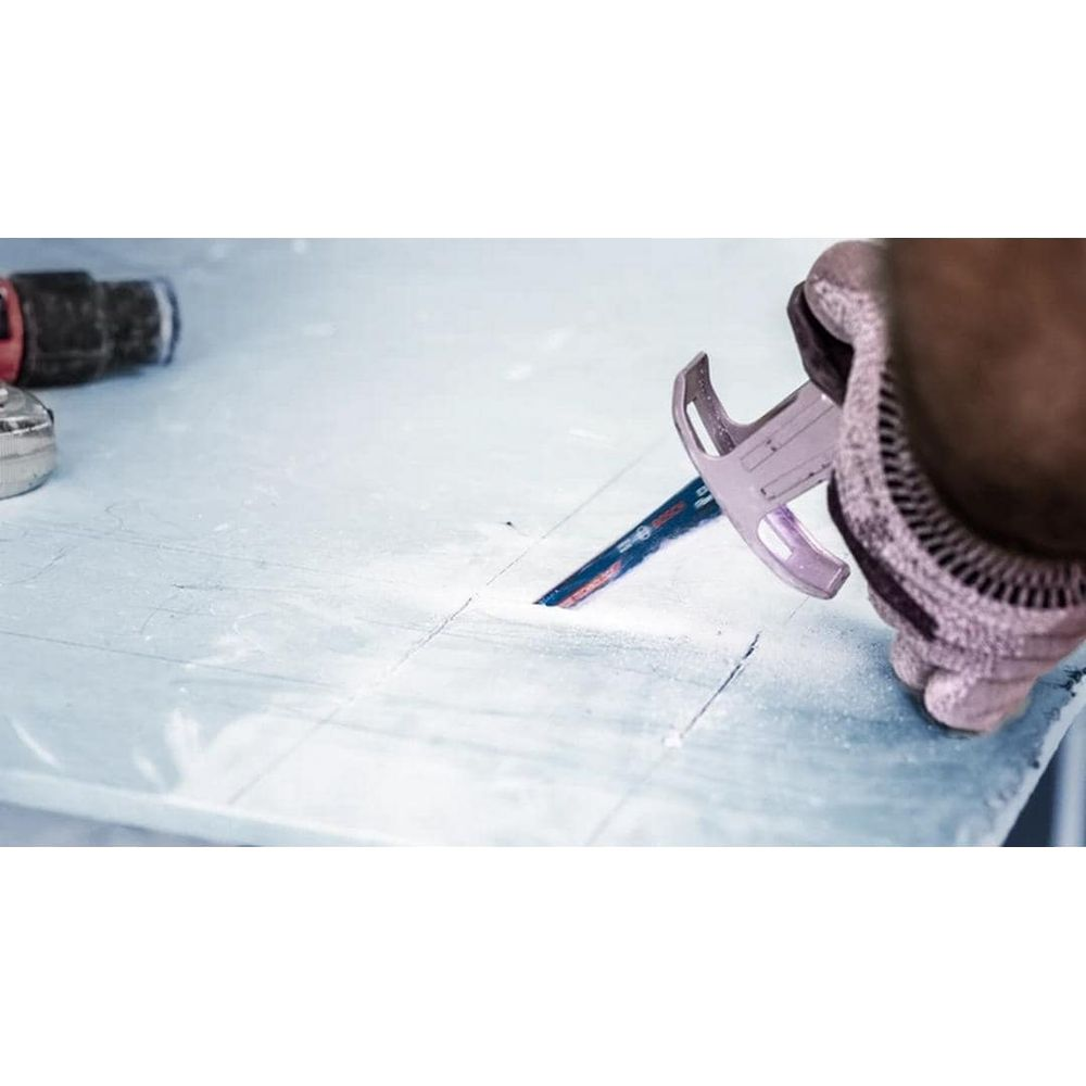 Rękawiczka z piłą ręczną przecina białą powierzchnię.