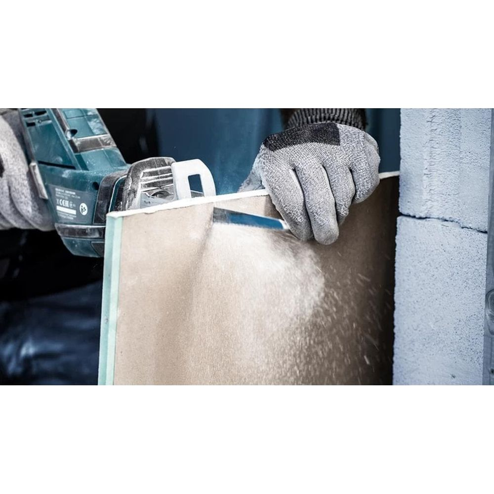 Osoba w rękawiczkach tnie płyty gipsowo-kartonowe piłą.