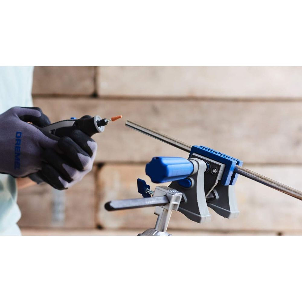 Een gehandschoende hand houdt een Dremel-gereedschap vast en bewerkt een metalen staaf in een bankschroef.