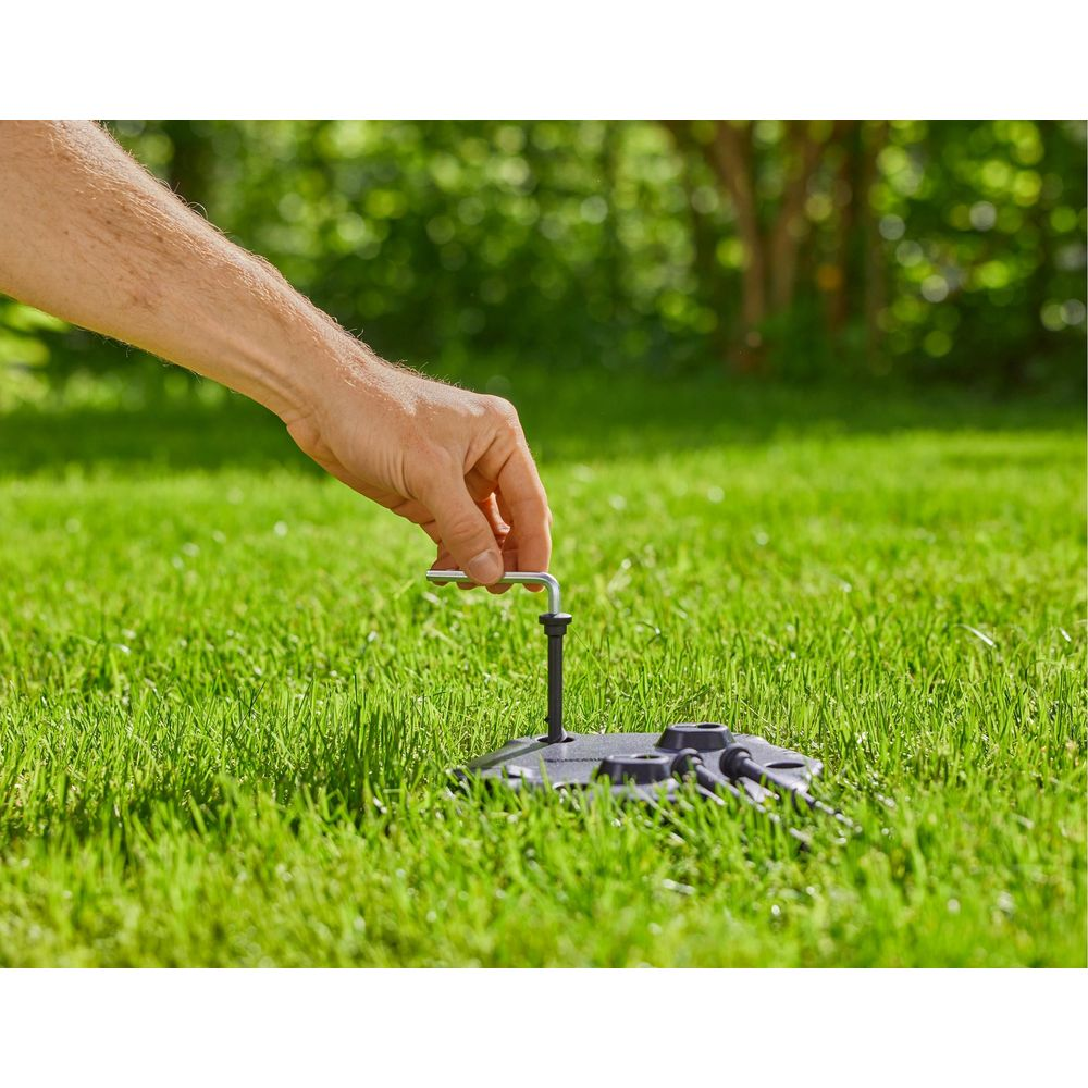 Eine Hand benutzt einen Inbusschlüssel, um einen schwarzen Gegenstand im Gras zu befestigen.