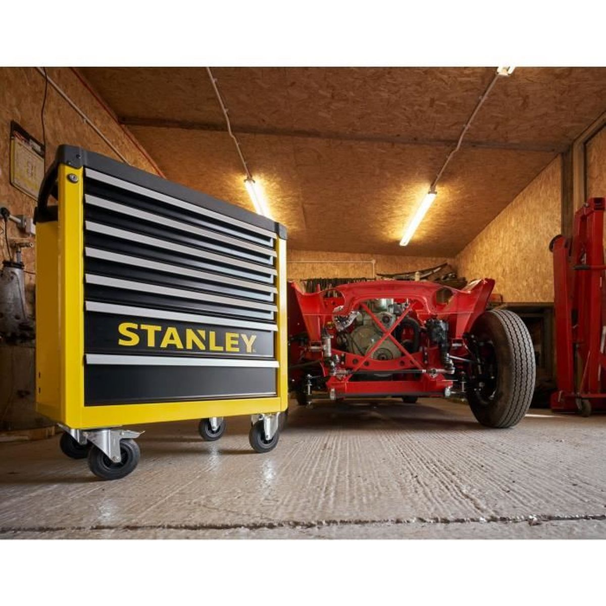 Un carrito de herramientas Stanley amarillo junto a un chasis de coche rojo.