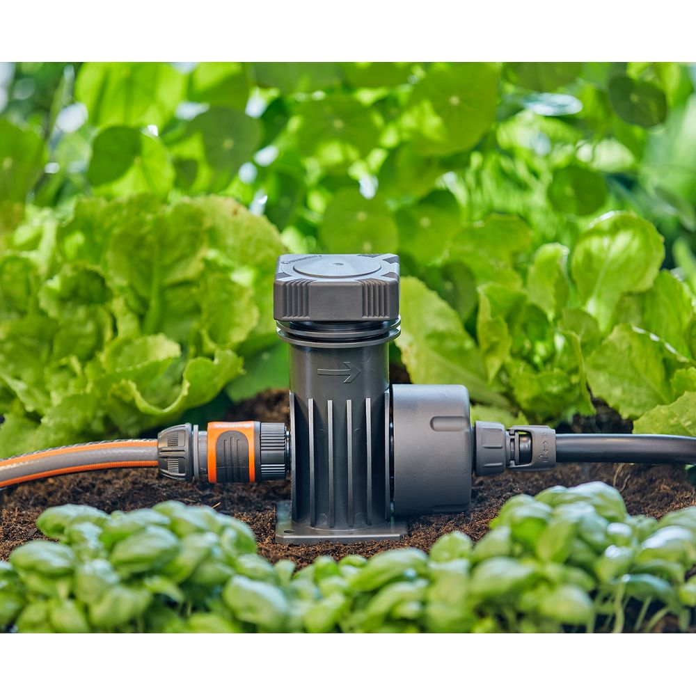 Ein schwarzer Gartenschlauchverbinder mit einem Schlauch und einem Tropfer im Beet.