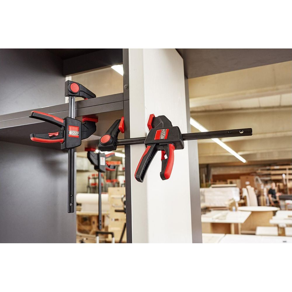 Deux serre-joints Bessey sur une étagère et un pilier dans un atelier.