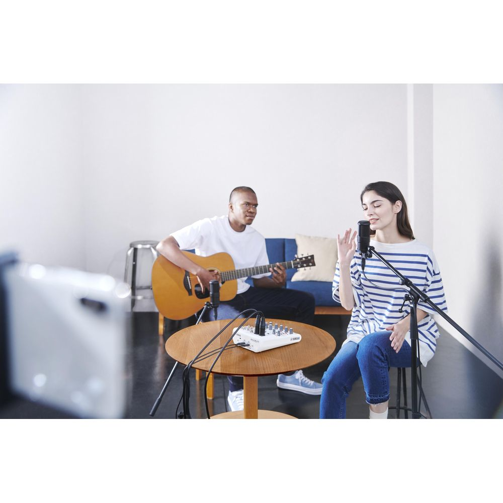 Uomo suona chitarra, donna canta in microfono, registratore su tavolo.
