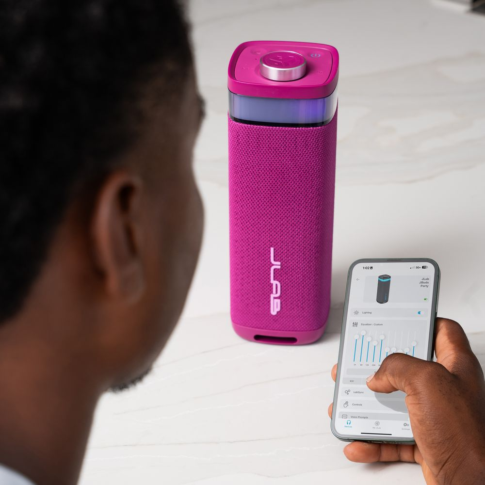 Personne utilisant un téléphone pour contrôler une enceinte rose avec lumières. Le téléphone affiche les réglages de l'égaliseur.