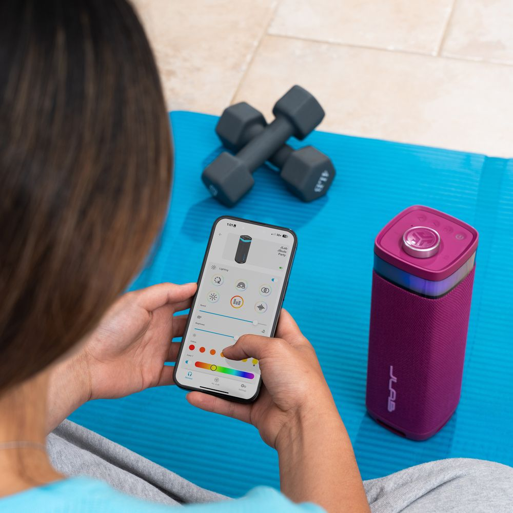 Personne utilise appli fitness sur smartphone près d'une enceinte violette et haltères.