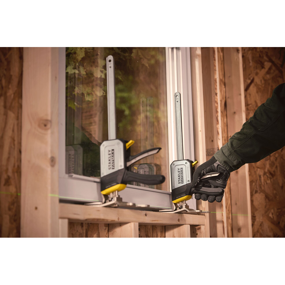 Ein Mann mit Handschuhen befestigt eine Klemme an einem Fensterrahmen, Holz im Hintergrund.