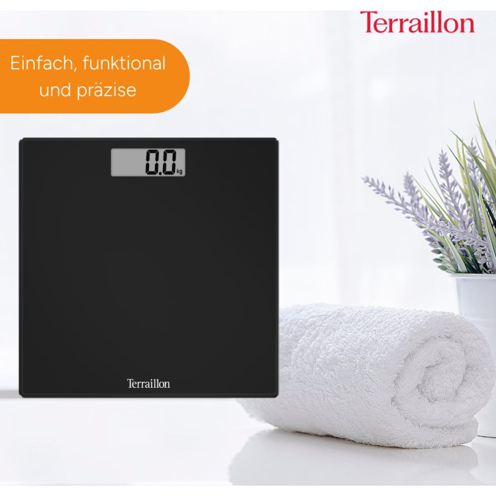 Czarna waga łazienkowa pokazująca 0,0 kg, obok zwiniętego białego ręcznika.