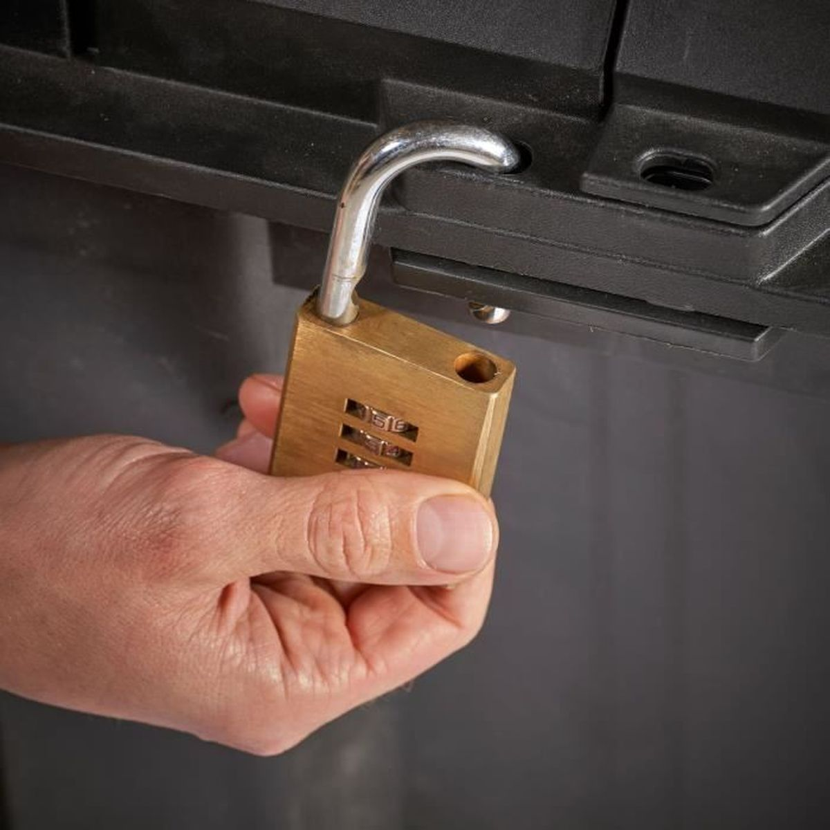 Een hand houdt een open, messing cijferslot vast.