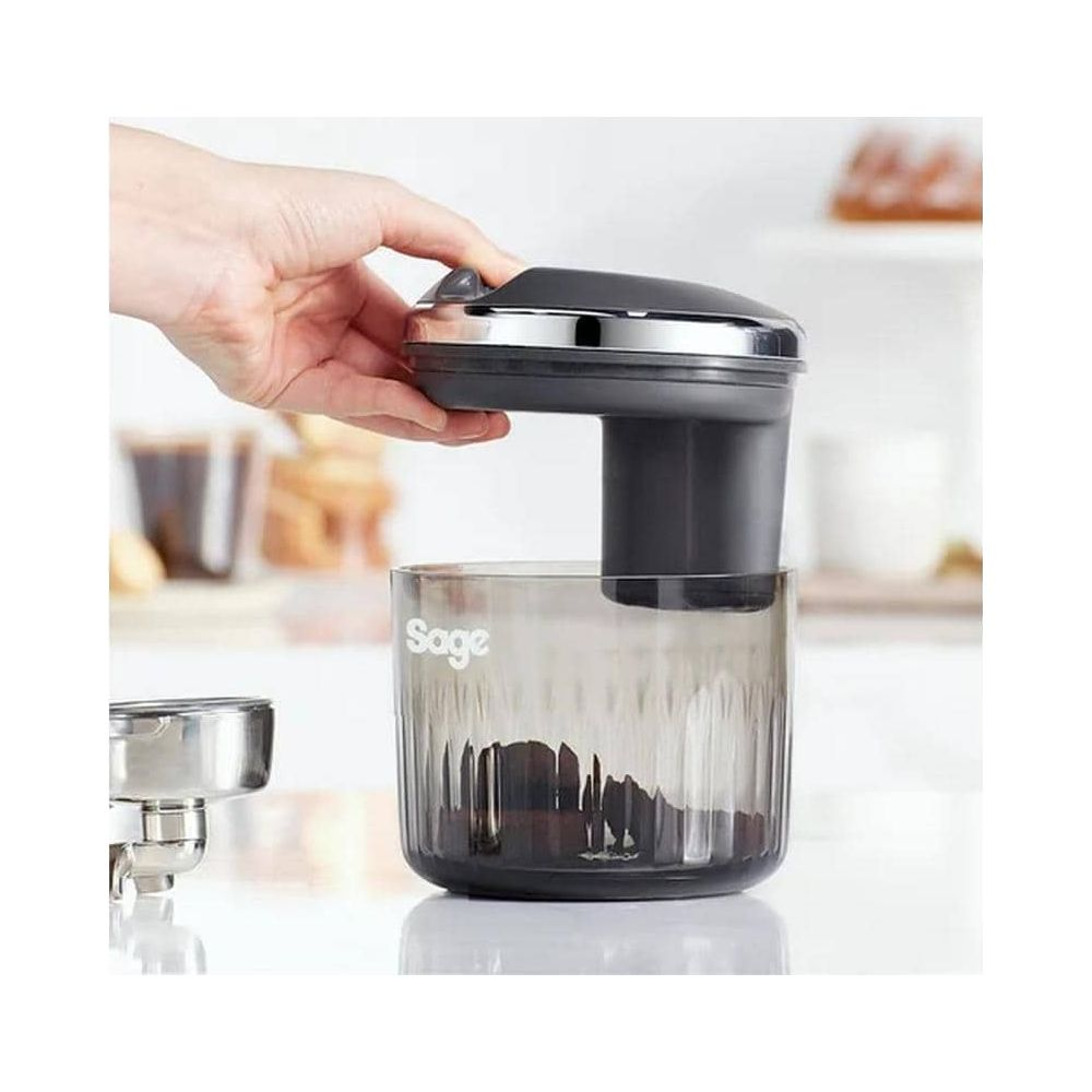 Una mano posiziona il coperchio su un contenitore grigio con fondi di caffè.