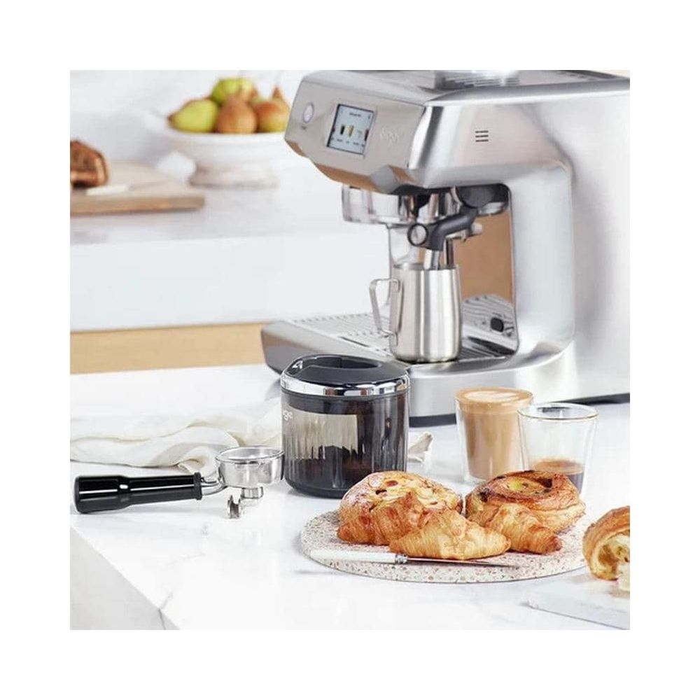 Una macchina da caffè argentata con pasticcini, caffè e frutta sullo sfondo.