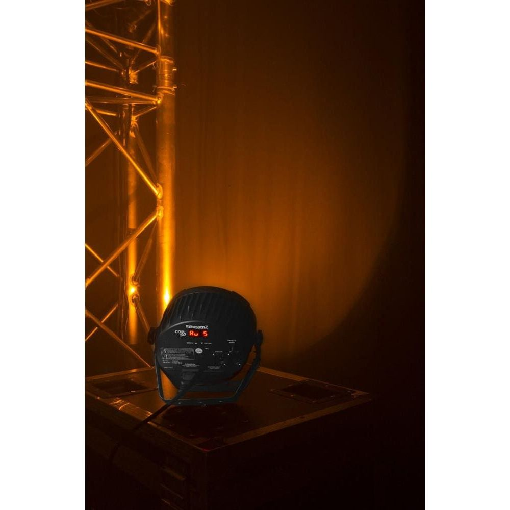 Una luz de escenario negra sobre una caja, iluminada por luz amarillo-naranja.