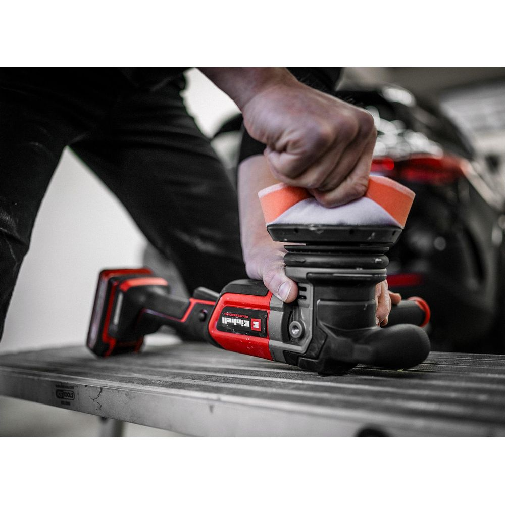 Personne polissant une voiture avec une polisseuse rouge et noire sur une table.