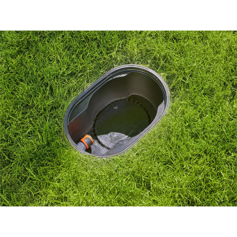 Ein schwarzer Rasensprengerbehälter mit einem orangefarbenen Schlauchanschluss, der im Gras liegt.