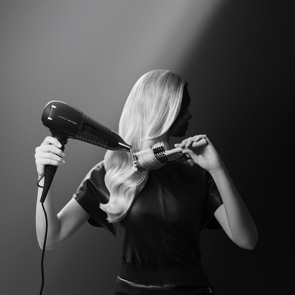 Kobieta suszy blond włosy czarną suszarką i okrągłą szczotką.