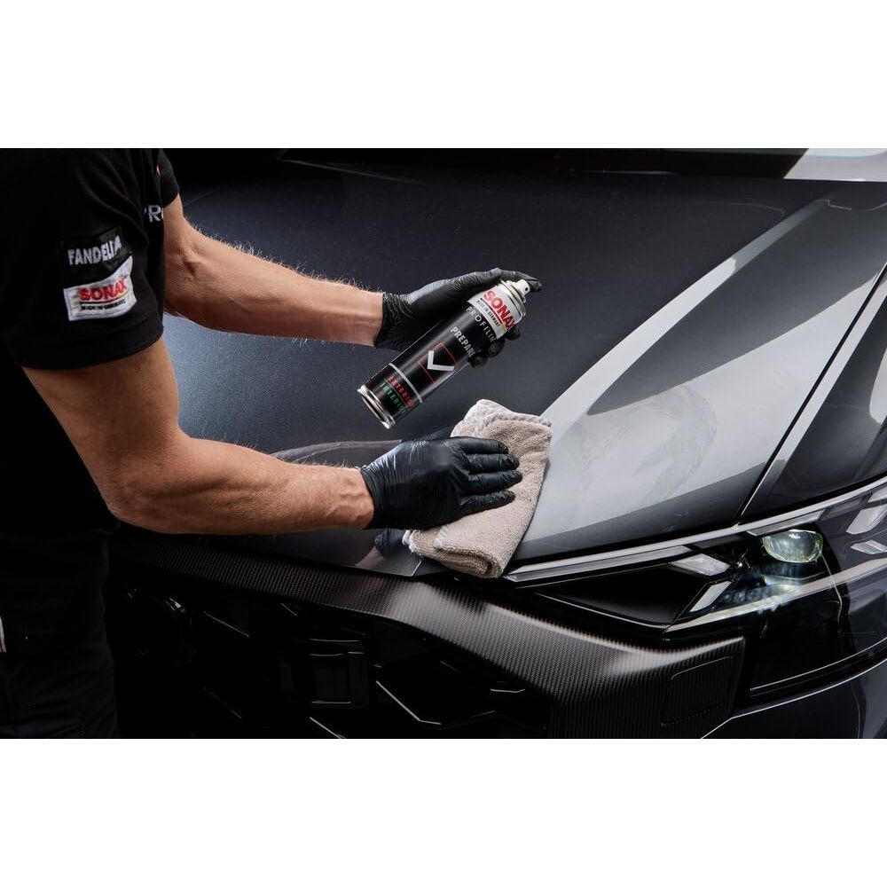 Person sprüht Autopflegeprodukt auf dunkle Motorhaube und wischt es mit Tuch ab.
